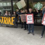 People carrying banners and picket signs pose in front of a Starbucks in downtown Portland